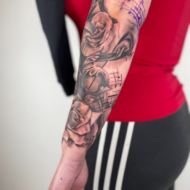 Tattooed Arm mit Rosenmotiven und musikalischen Elementen, nah an der Haut.