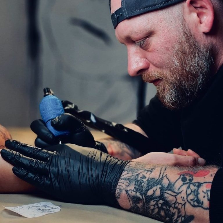 Teambild Ein tätowierter Mann tätowiert mit einer Maschine einen Arm.